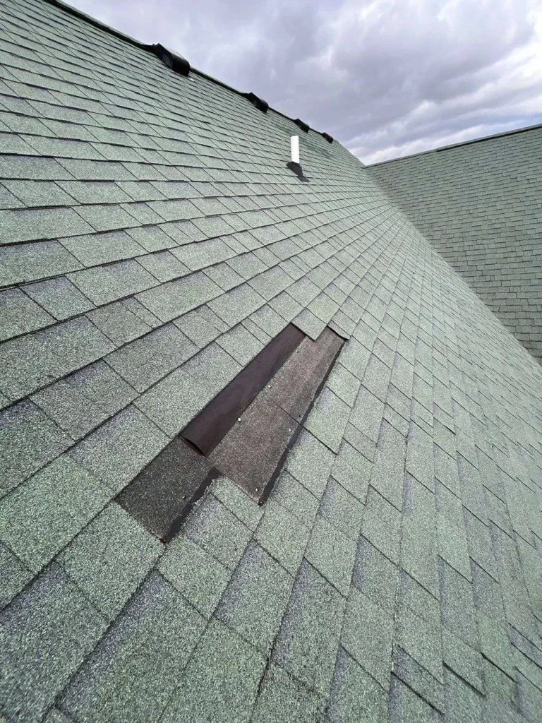 Close-up of a green shingle roof with visible damage and missing shingles, showcasing the need for roof damage repair by a commercial roofing contractor.