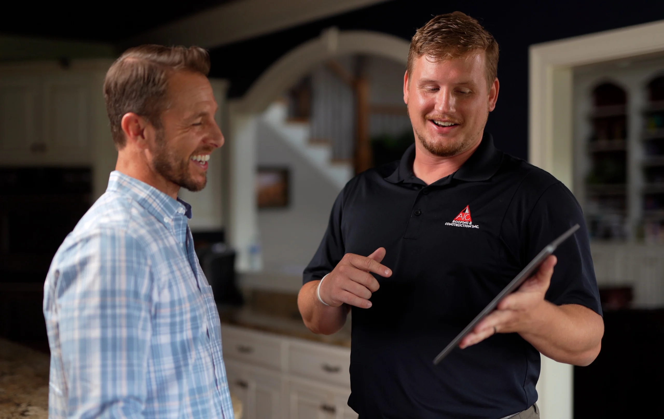 Customer viewing AIC Roofing and Construction's 4.9-star Google reviews on a smartphone. A roofing contractor from AIC Roofing discussing roof replacement options and warranties with a homeowner in their kitchen.