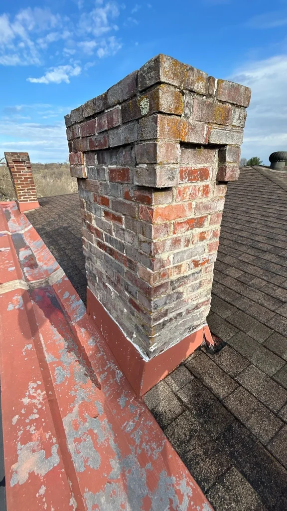 Old brick chimney with deteriorated flashing contributing to a visible roof leak on an asphalt shingle roof in Louisville.