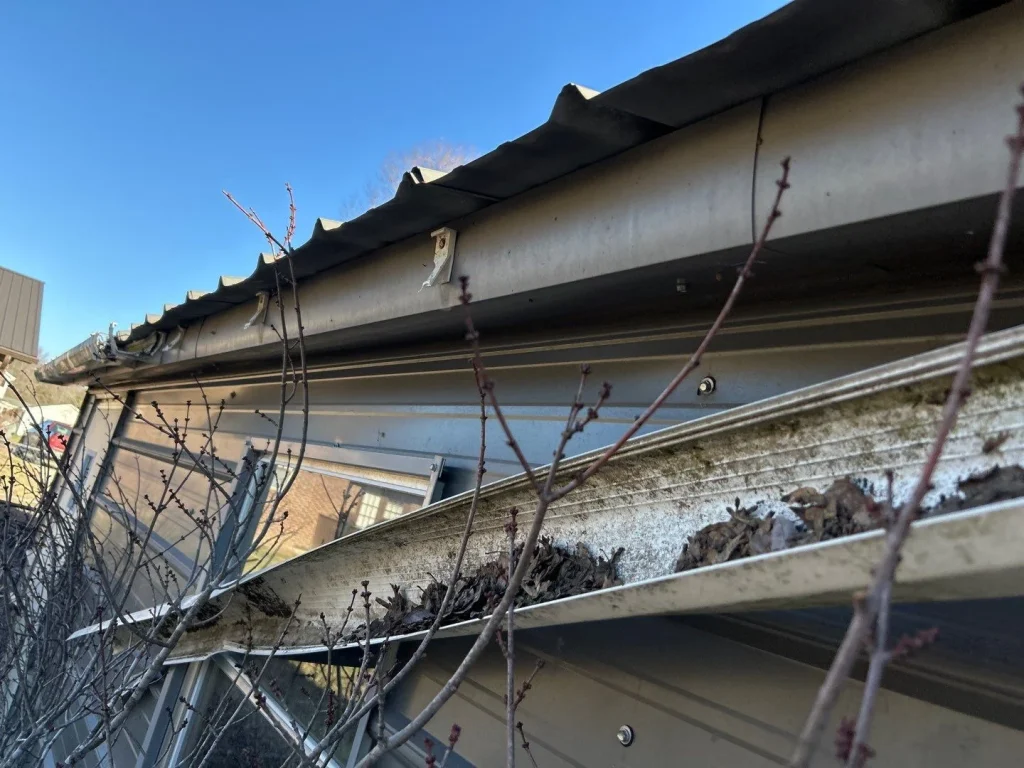 Clogged and sagging metal gutters with debris and bent hangers on a building in Richmond, KY