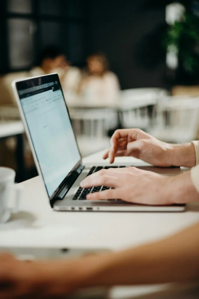 Working on a Laptop in a Modern Café Setting Close-up of a person typing on a laptop at a white table in a cozy cafe.