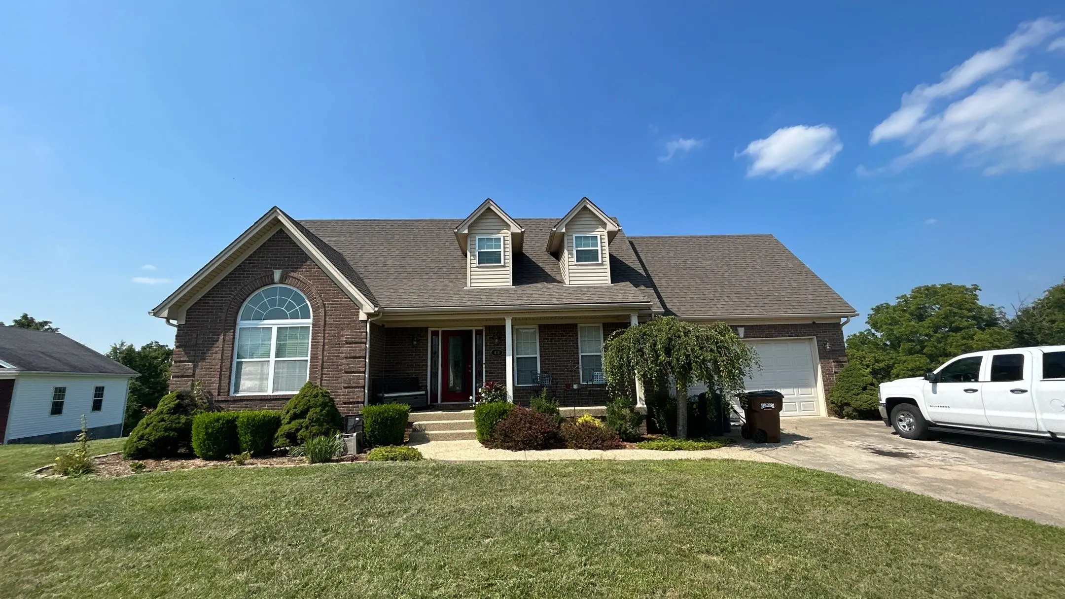 Brick two-story home in Taylorsville, KY with gabled roof, dormer windows, and manicured front lawn under a clear blue sky.