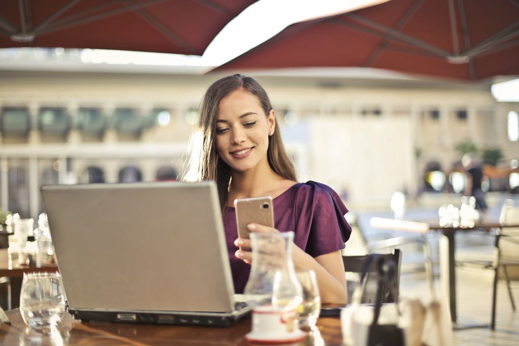 Confident Professional at Work in a Bright Modern Office Woman enjoying remote work at a café, using a laptop and smartphone.