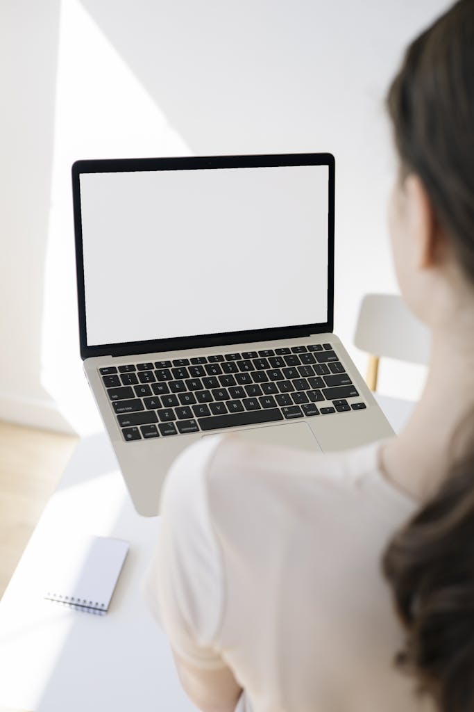 Adult woman in white t-shirt using a blank laptop screen at a modern workspace.