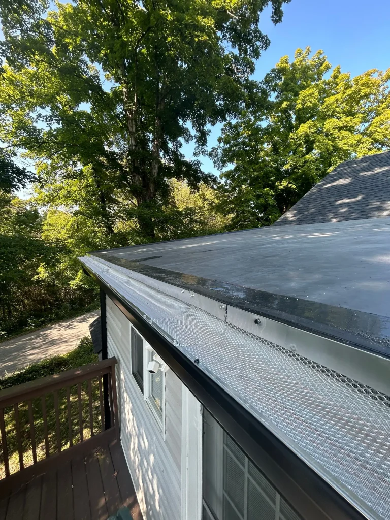 Close-up of newly installed gutter guard on a Kentucky home by AIC Roofing & Construction, with trees and a driveway in the background.