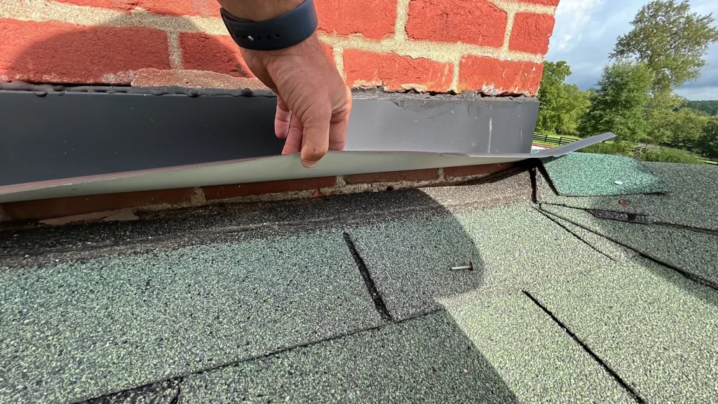 Close-up of a roof repair showing lifted flashing around a brick chimney on a Simpsonville, KY home by AIC Roofing & Construction.