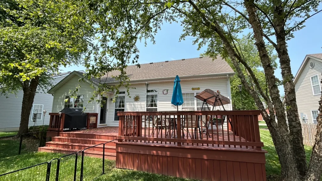 Back view of a Simpsonville, KY home with light-colored siding installed by AIC Roofing & Construction, featuring a red wooden deck and patio furniture.