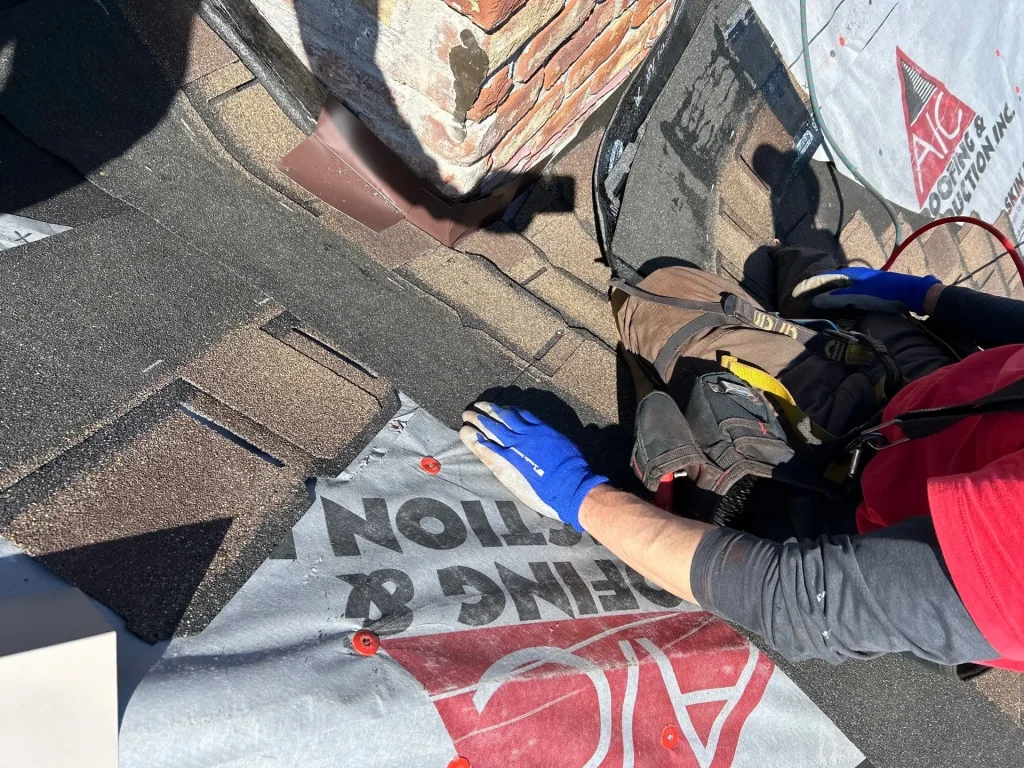 Roofer repairing flashing and installing shingles near a chimney in New Albany, IN for AIC Roofing & Construction.
