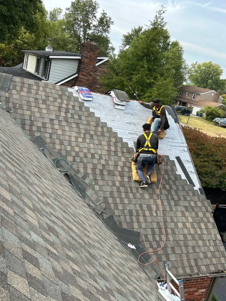 Two roofing contractors installing new shingles on a steep roof during a repair by AIC Roofing & Construction.