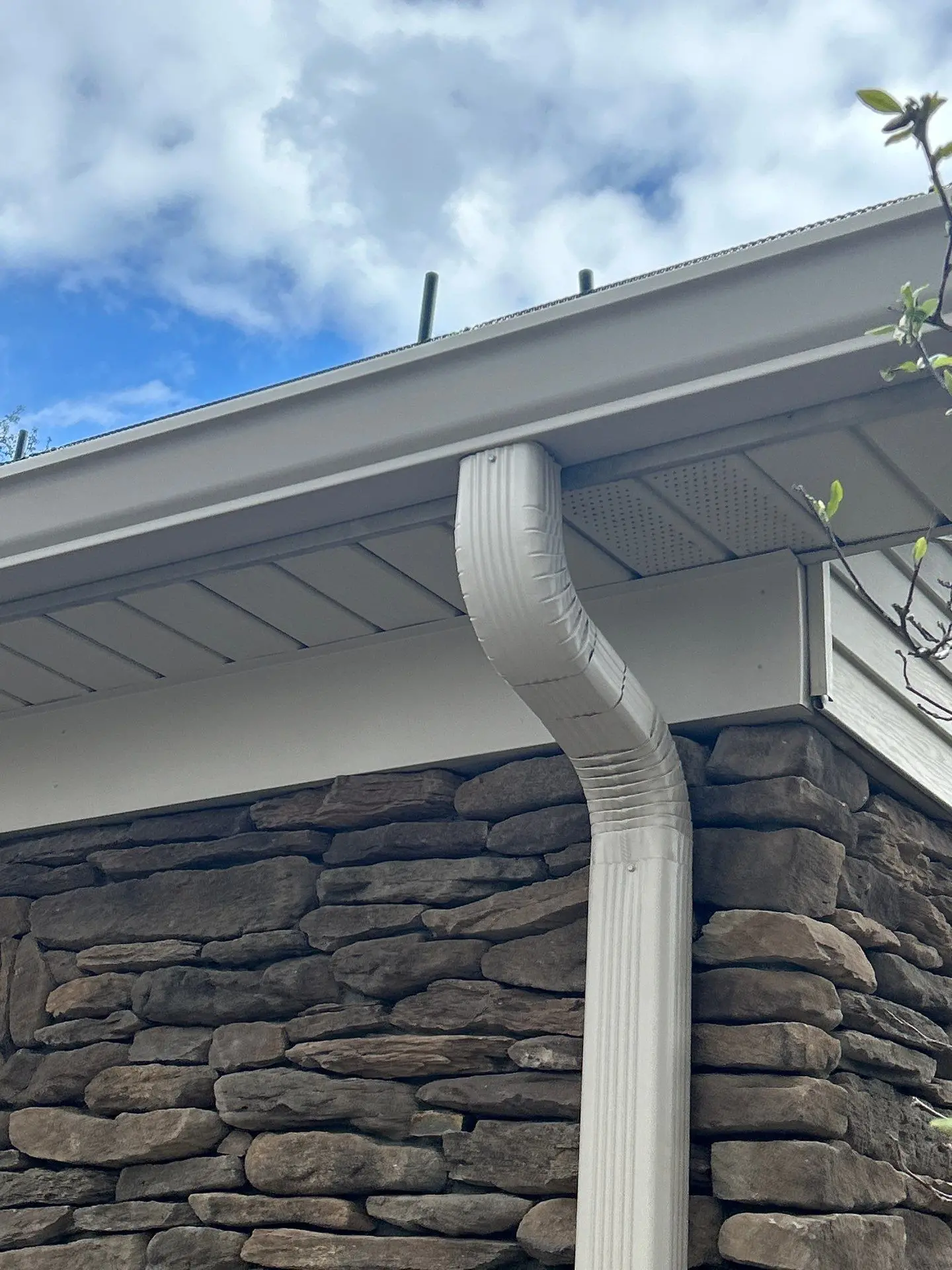 Newly installed white gutter system on a stone exterior home by AIC Roofing & Construction