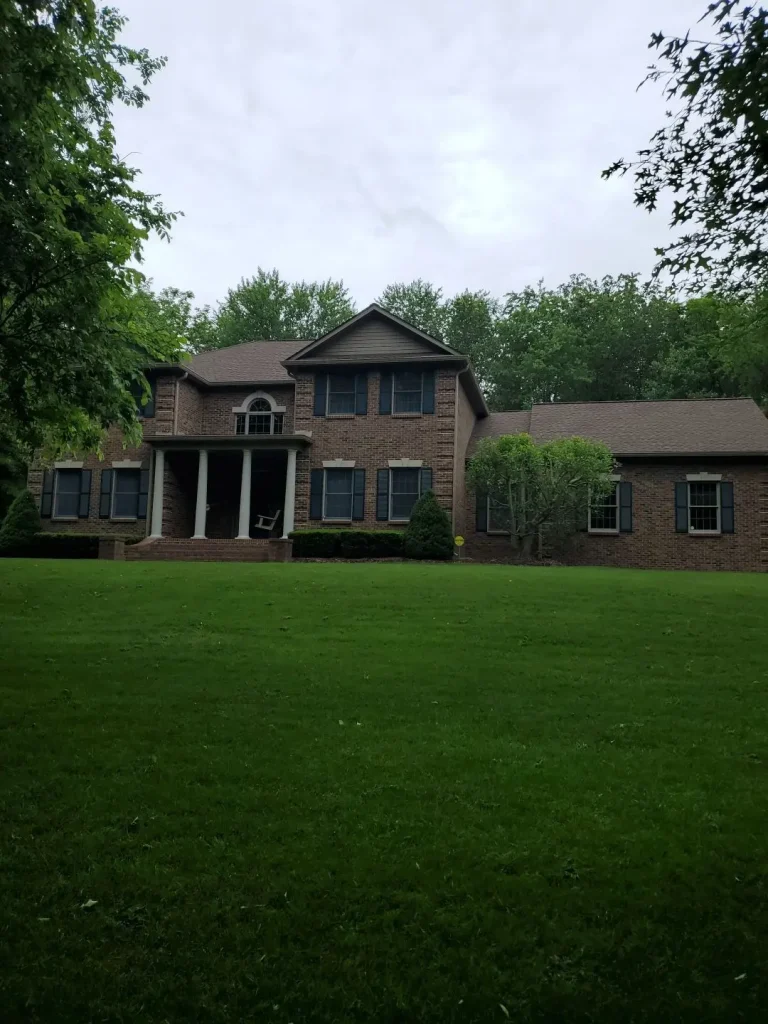 Two-story brick home with new roof replacement by AIC in Wilmore, KY, surrounded by lush trees and a well-maintained front lawn.