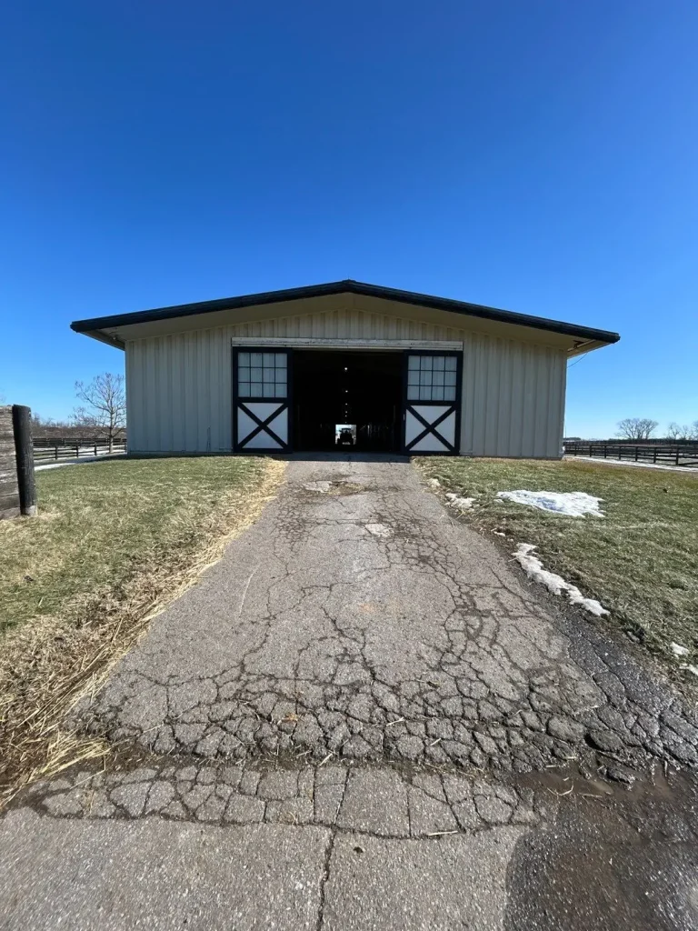 Barn in Lexington, KY with a newly replaced roof, shown from the entrance with a cracked asphalt driveway.