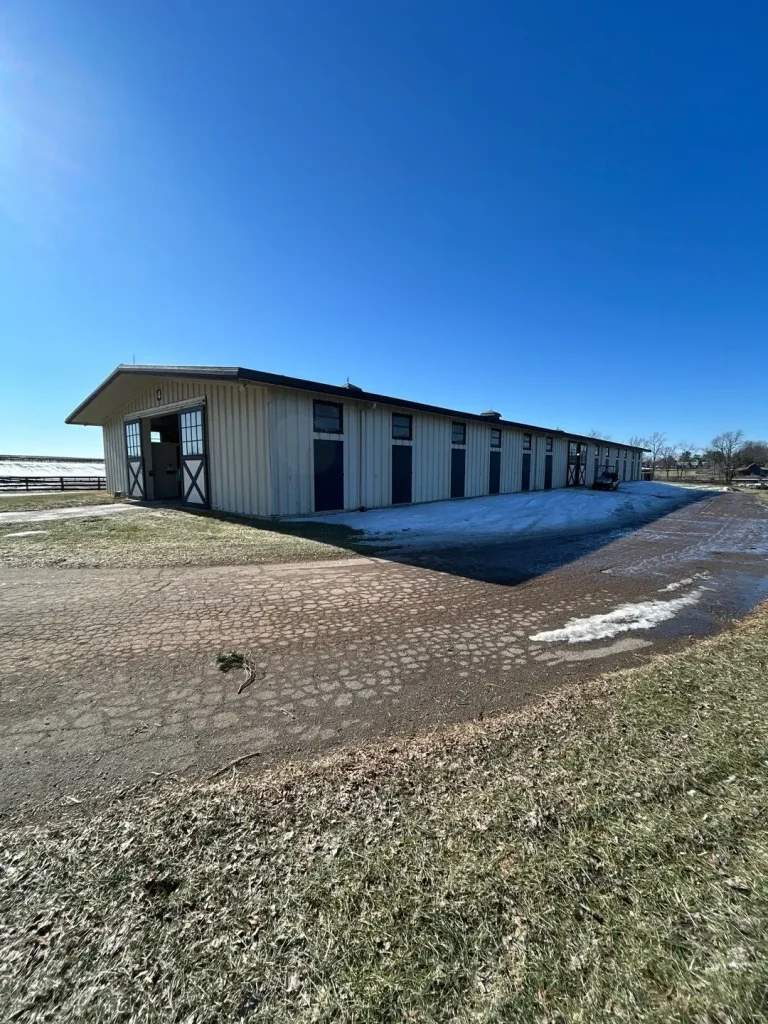Long cream-colored barn in Lexington, KY with a new dark roof installed by AIC Roofing & Construction.