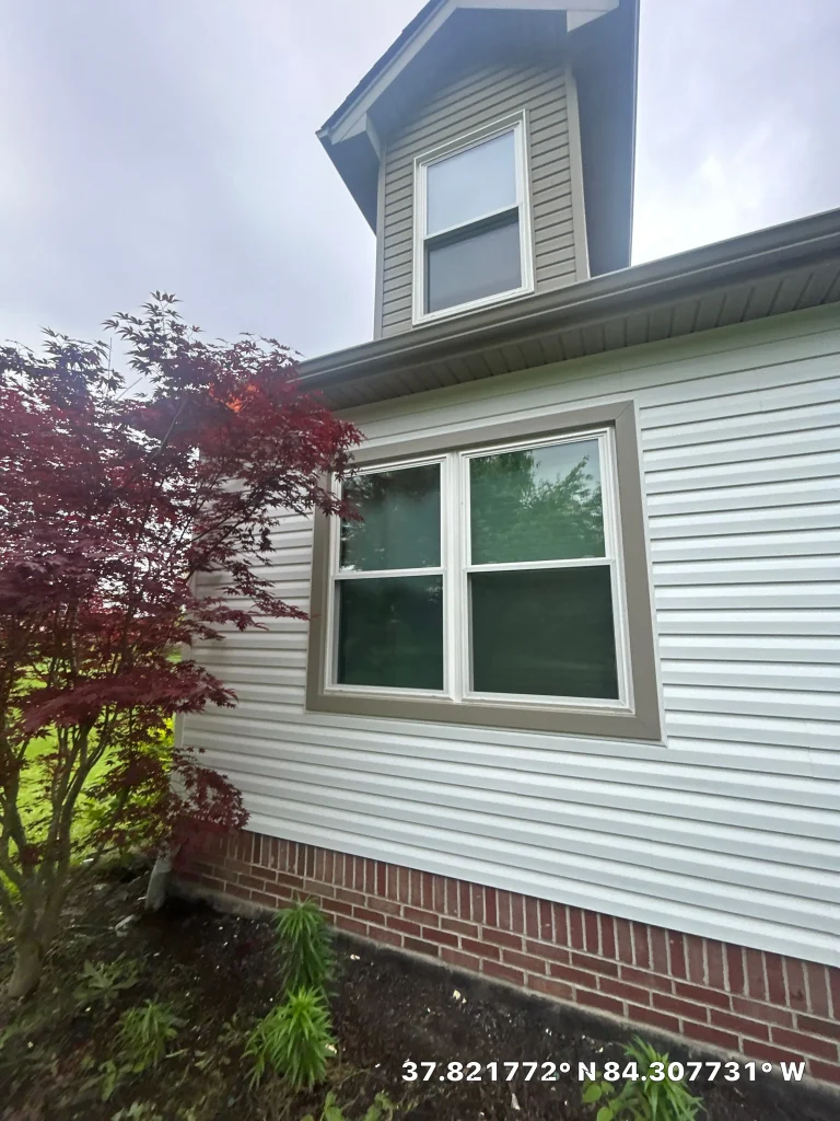 Side view of a Richmond home with new white vinyl siding and a brick foundation installed by AIC Roofing & Construction.