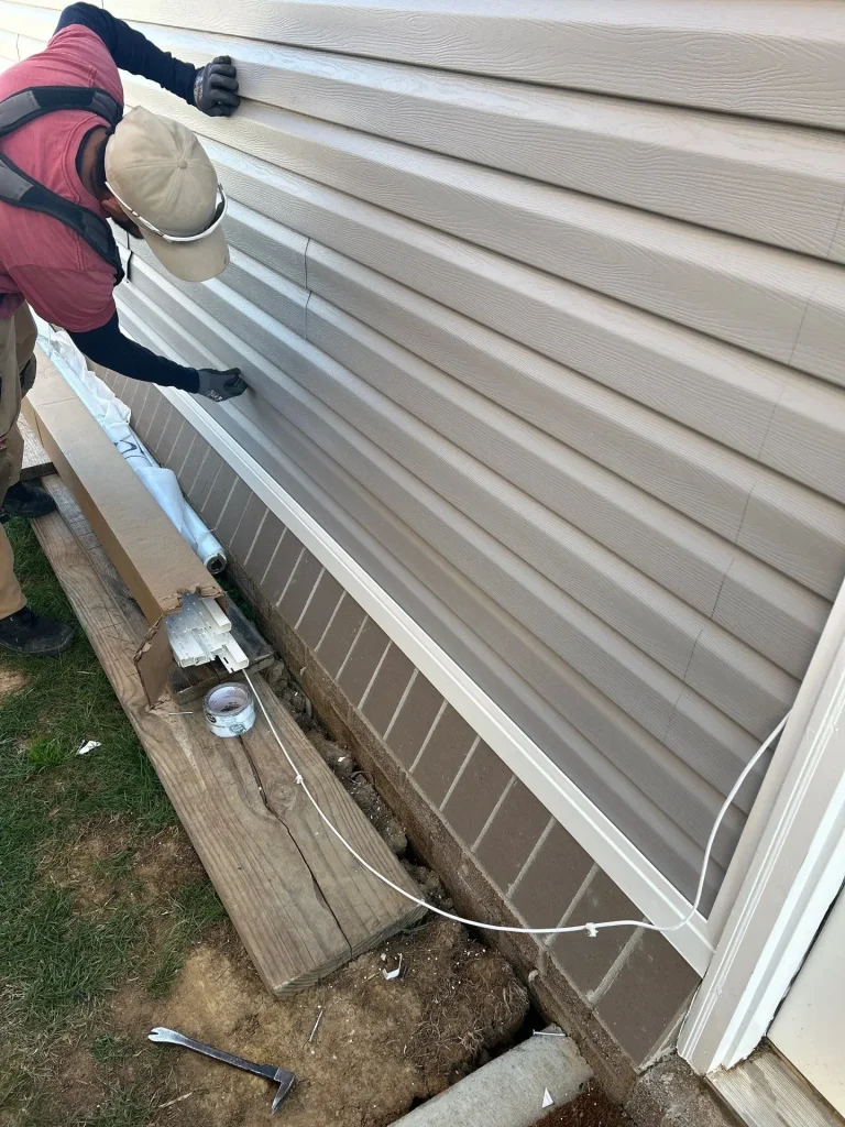 AIC Roofing & Construction crew member installing beige siding on a Richmond home.