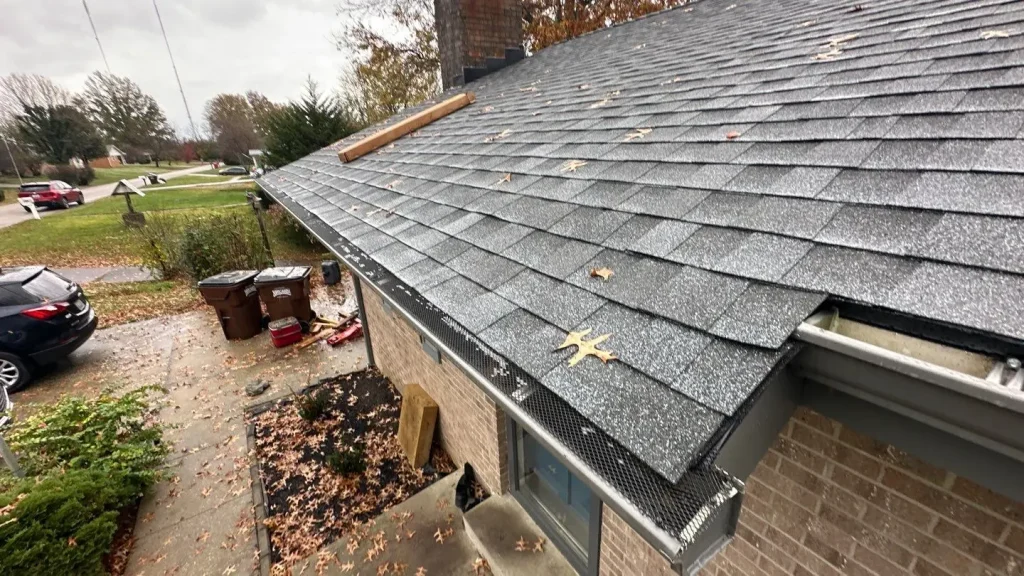 Newly installed gutter guard system on a  home by AIC Roofing & Construction, with leaf debris visible on the roof.