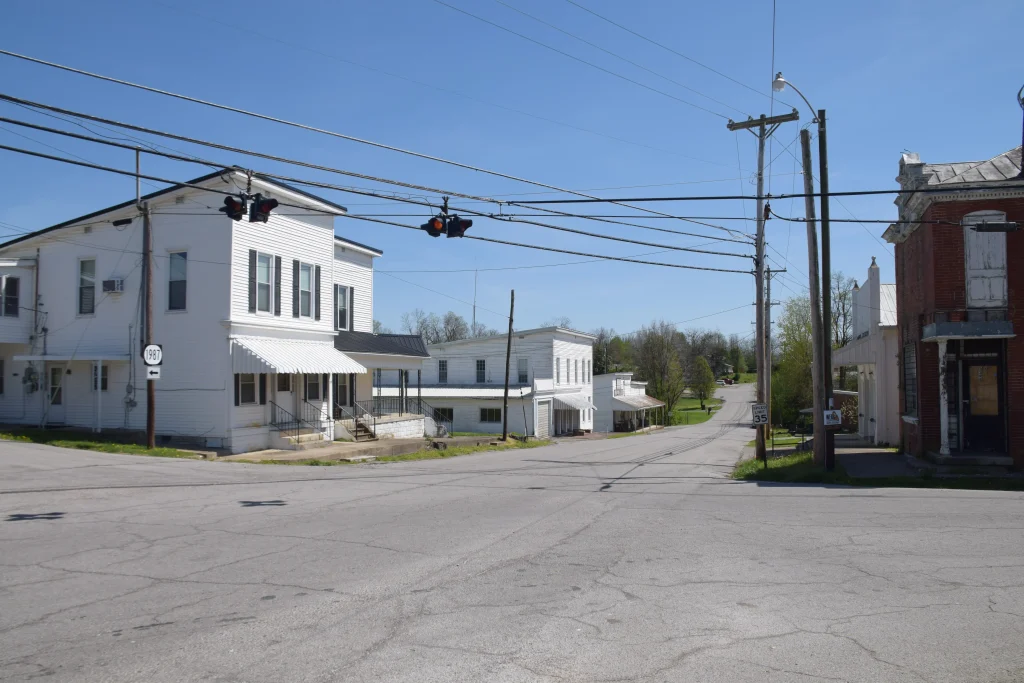 Street view of a quiet intersection in Salvisa, KY featuring historic white wooden buildings and a red brick structure under a clear blue sky.
