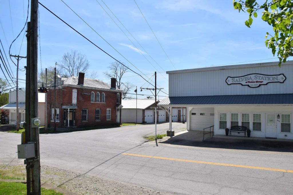 A street corner in Salvisa, KY featuring Salvisa Station, a historic brick building, and the Salvisa Fire Department under a sunny sky.