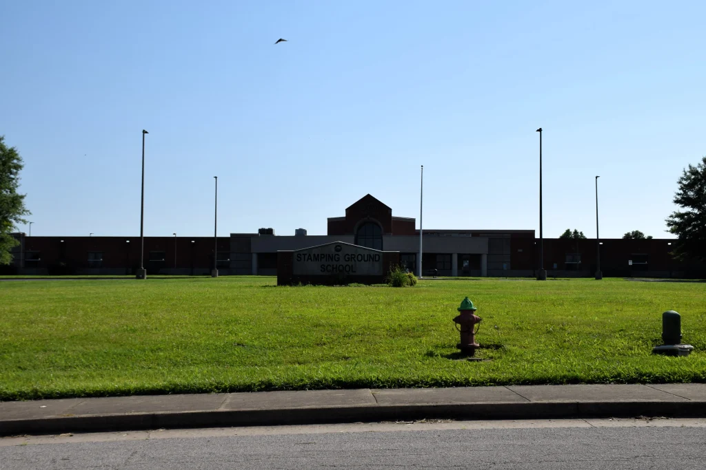 Front view of Stamping Ground School with a large lawn and fire hydrants in the foreground.
