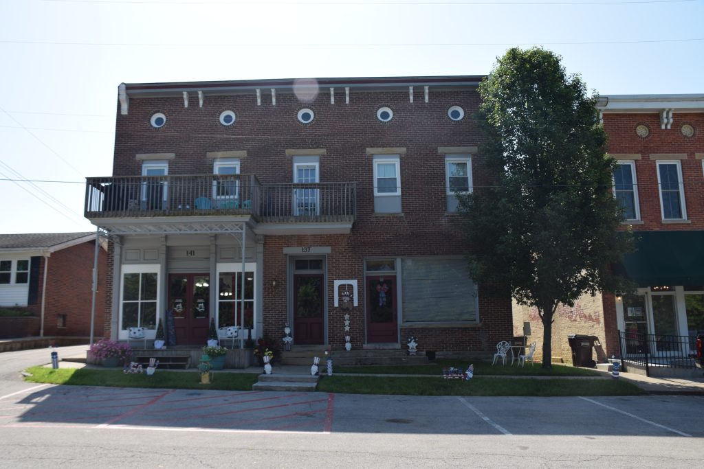 Historic two-story brick building with upper balconies, circular windows, and patriotic decorations along a quiet street.