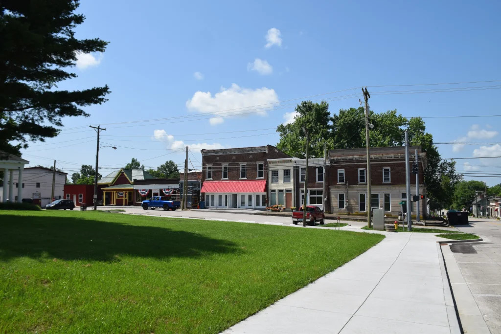 Historic buildings and small businesses along a sunny street in downtown Millersburg, KY, viewed from a nearby sidewalk and green space.