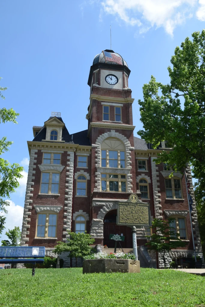 Historic courthouse building with a clock tower in Carlisle, Kentucky, surrounded by green trees and a clear blue sky.