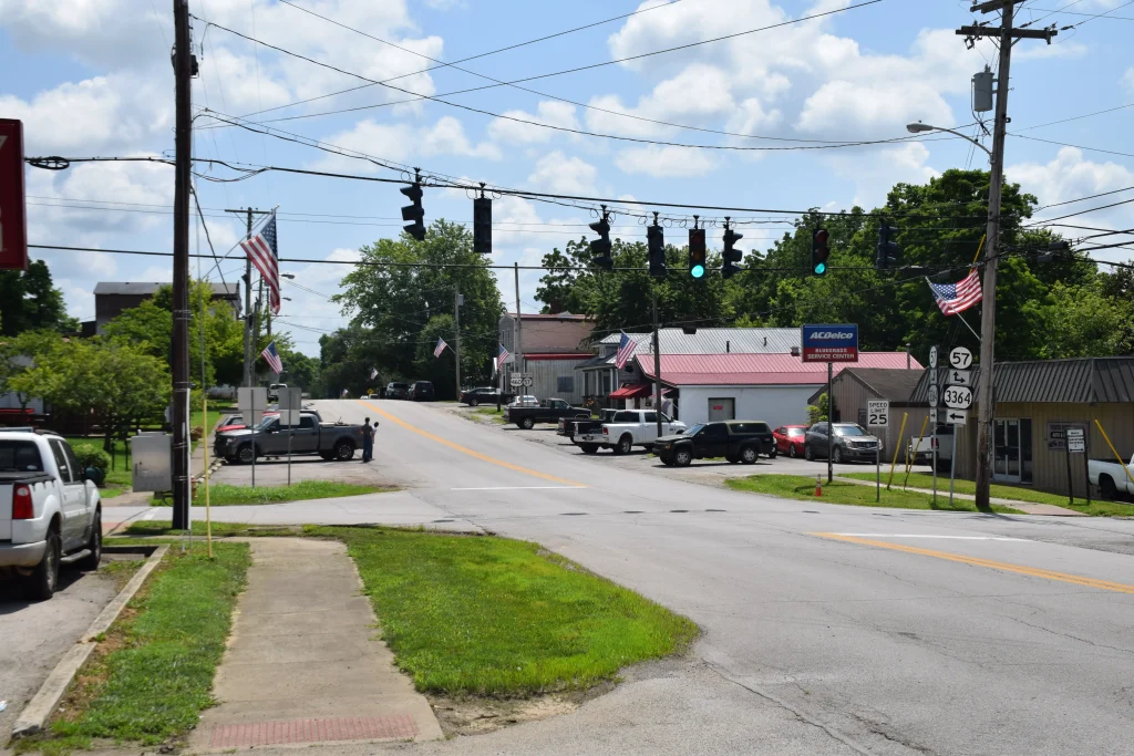 Main intersection in North Middletown, KY, with traffic lights, American flags, local businesses, and parked vehicles.