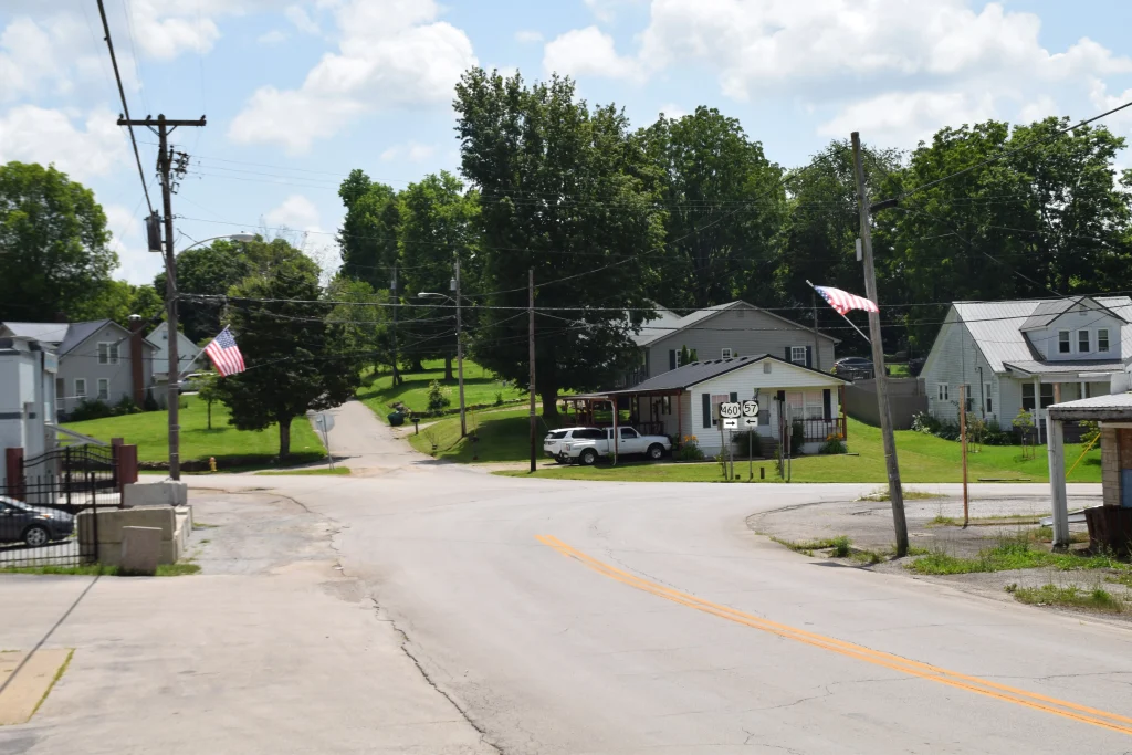 Street view of a quiet residential intersection in North Middletown, KY, with American flags, small homes, and road signs for Routes 460 and 57.