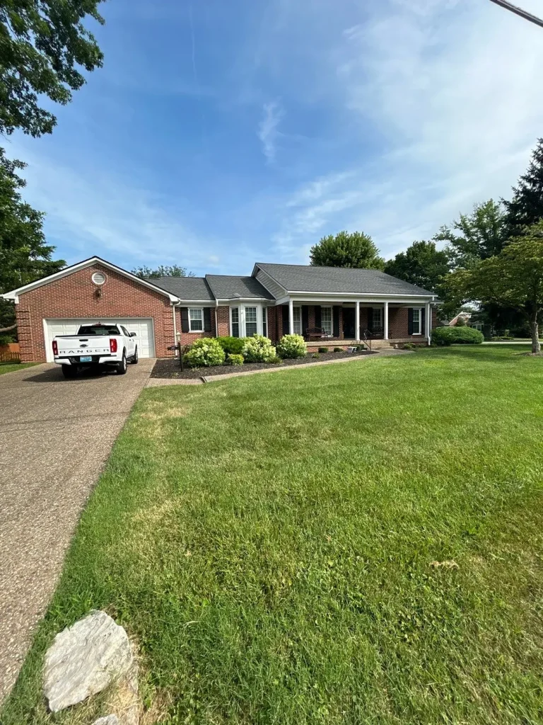 New roof replacement on a red brick home in Westport, KY completed by AIC Roofing, featuring dark shingles and a well-manicured lawn.