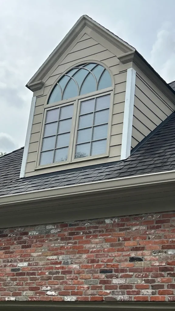 Close-up of new beige siding and decorative arched window installed above a brick wall on a home in Fisherville, KY by AIC Roofing.