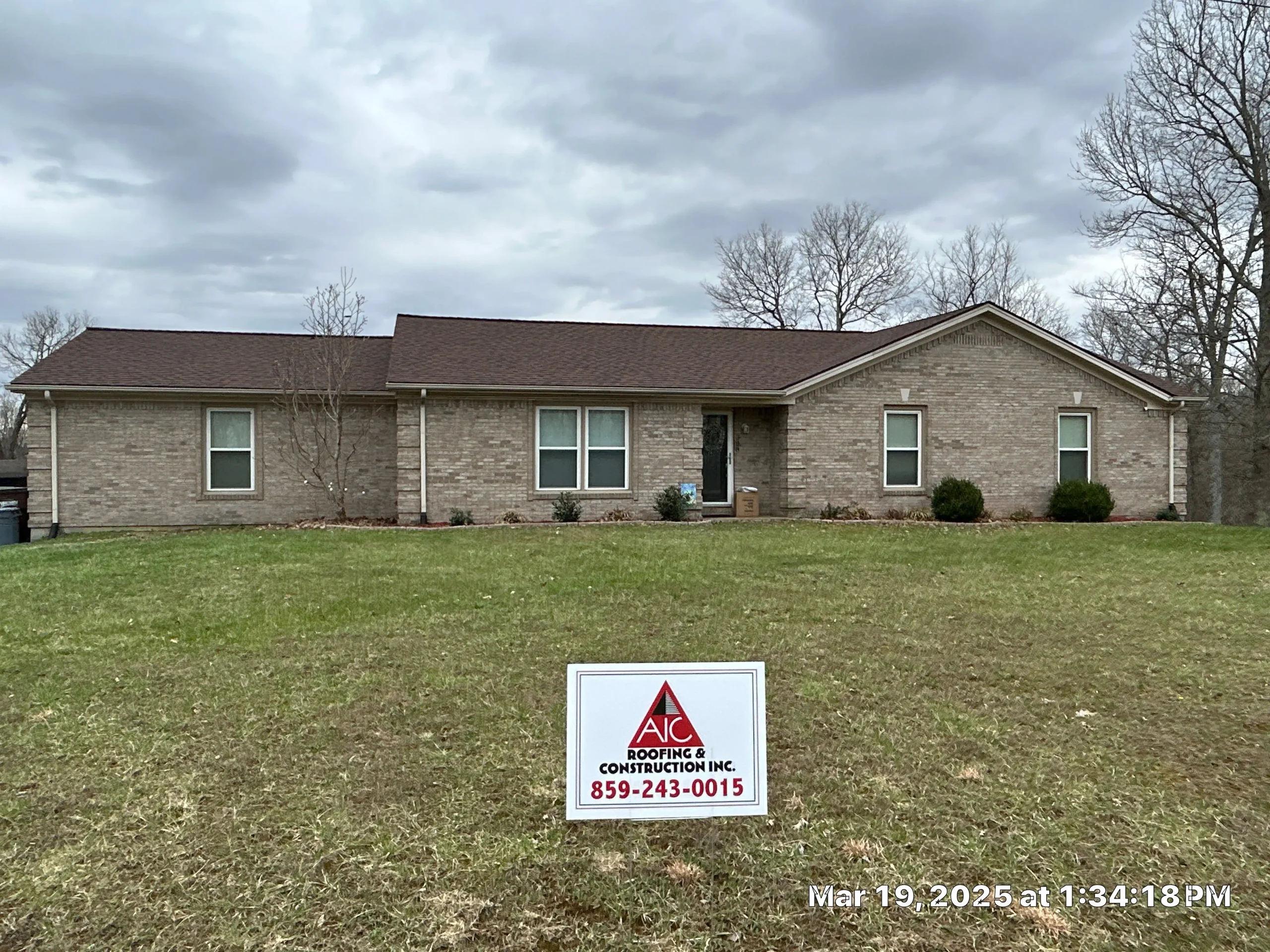 A single-story brick home in Sadieville, KY with a new roof installed by AIC Roofing & Construction, featuring a sign in the yard.
