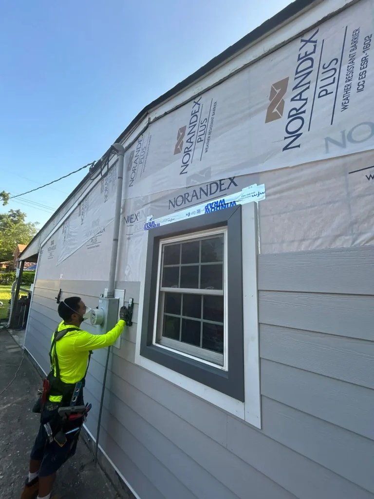 Crew member installing new gray siding on a Lexington, KY home with Norandex weather barrier visible.