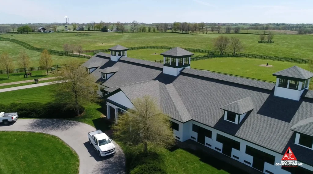 Large white barn with fresh asphalt roofing and cupolas, surrounded by green pastures in Kentucky, completed by AIC Roofing & Construction.