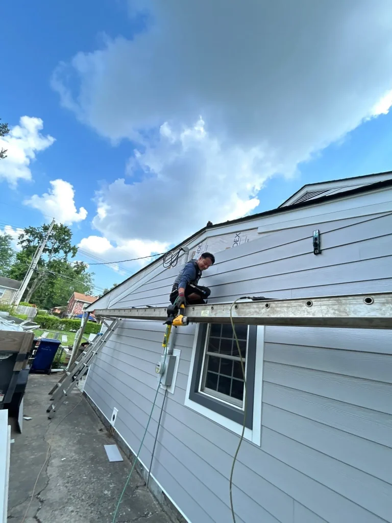 A crew member from AIC Roofing & Construction installs new siding on a Lexington, KY home while working from a ladder on the side of the house.