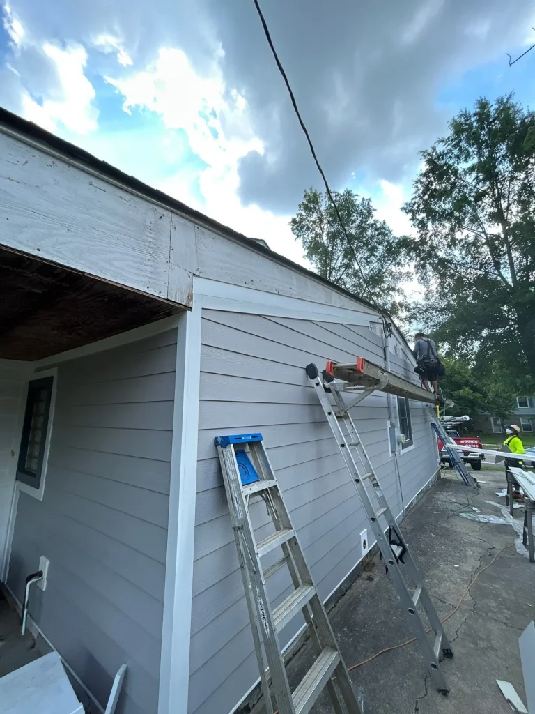 Construction crew working on siding installation and fascia repair on a residential home with ladders and tools set up.