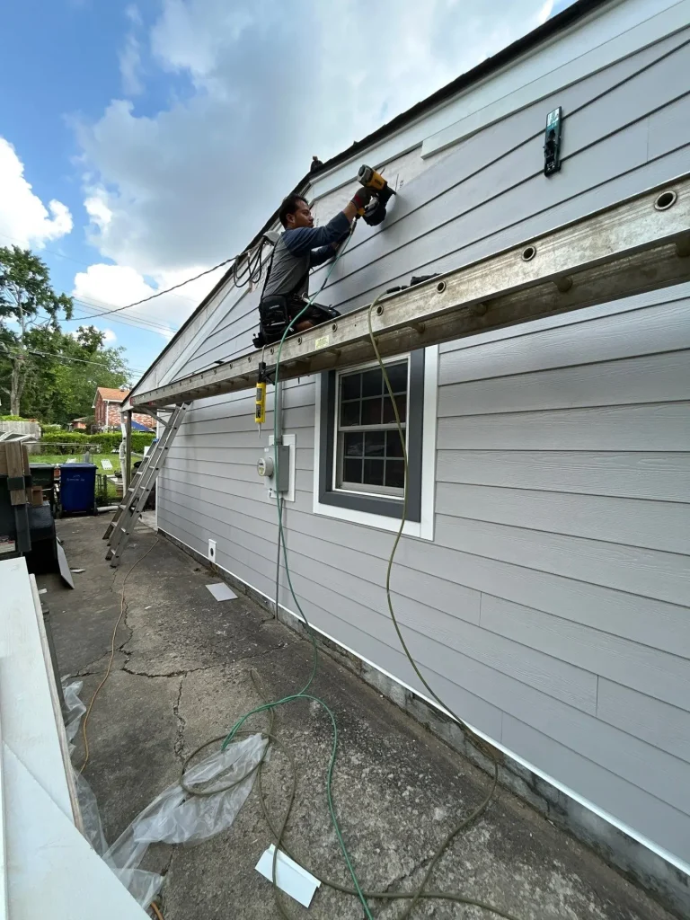 AIC crew member installing new gray siding on a Lexington, KY home using a nail gun while working from a secured ladder.