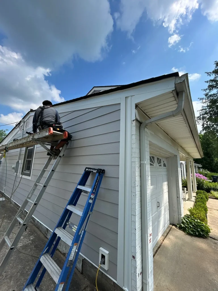 AIC crew member installing new gray siding on a Lexington, KY home using a ladder and safety gear.