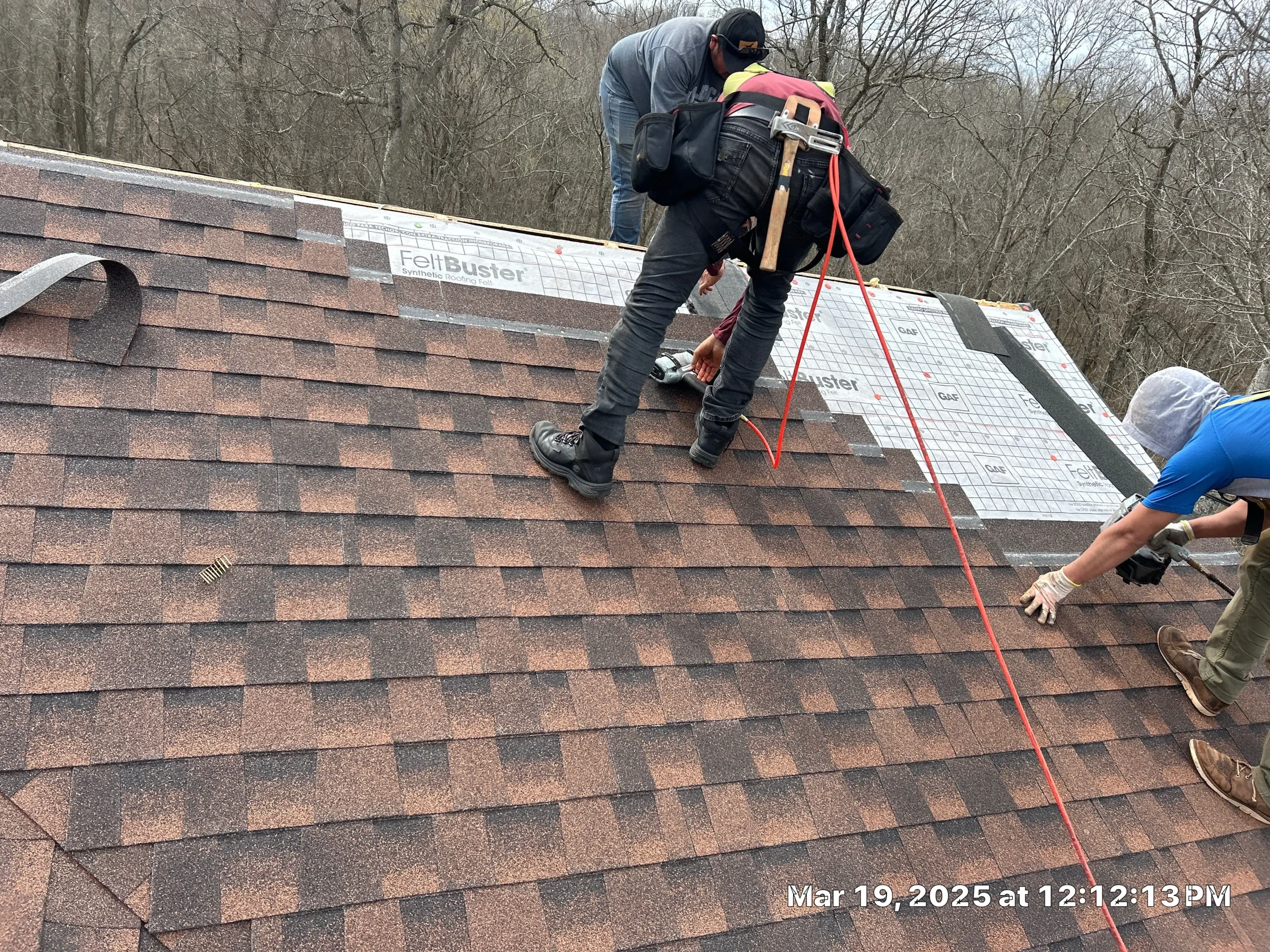 Three AIC crew members installing shingles on a residential roof in Sadieville, KY, using safety harnesses and synthetic underlayment.
