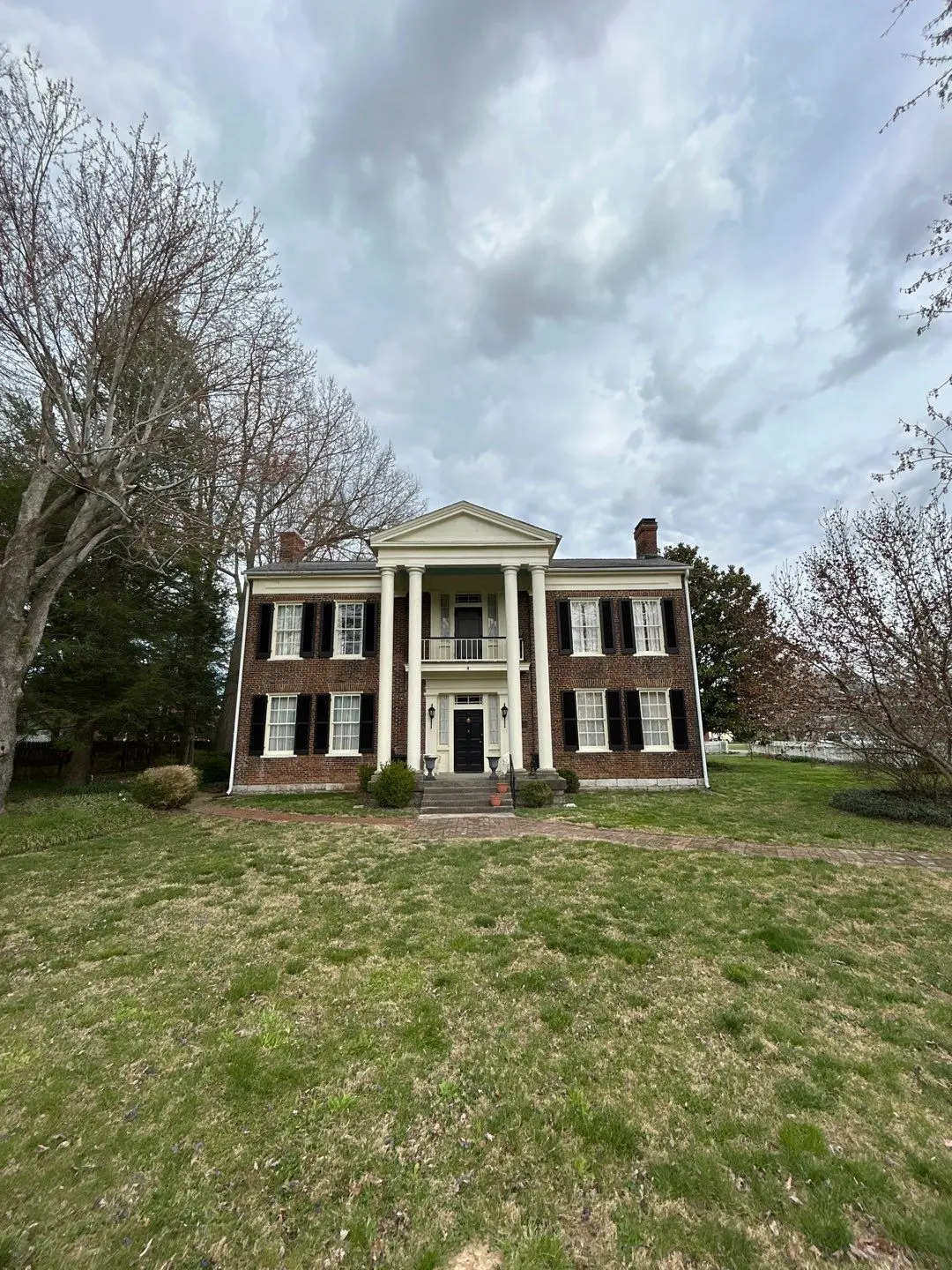 Historic brick home in Perryville, KY with a newly installed roof by AIC Roofing & Construction, featuring white columns and black shutters.