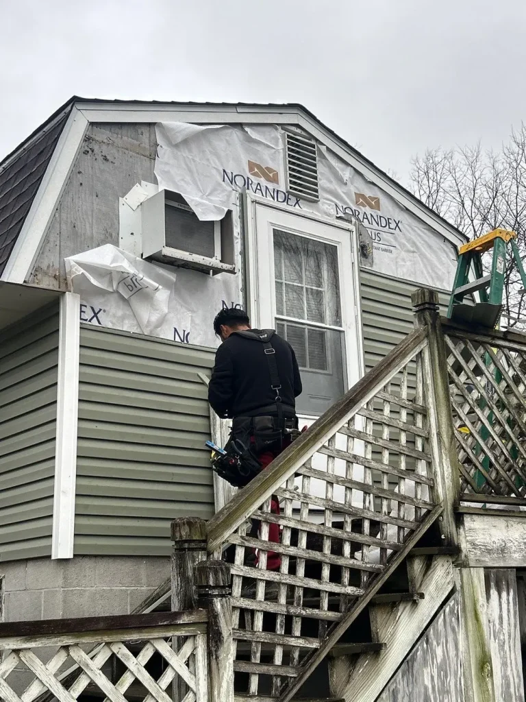 A construction worker installs new green vinyl siding on the upper level of a home during a renovation project.