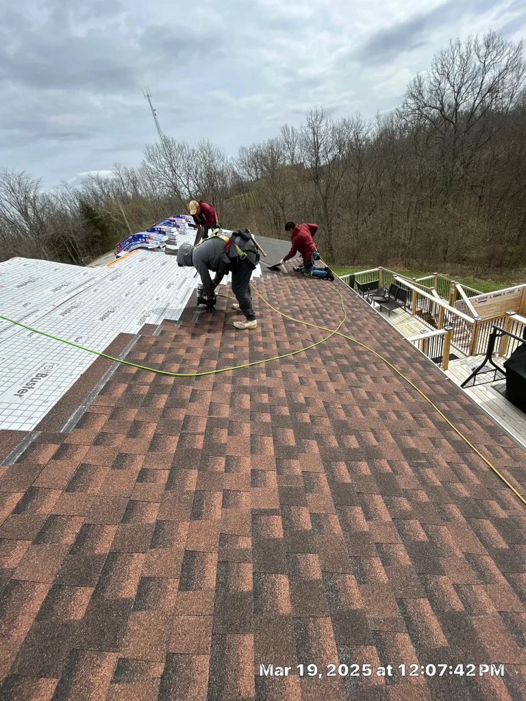 AIC Roofing crew members repairing a roof in Lexington, KY, installing shingles and underlayment on a steep slope using safety harnesses.