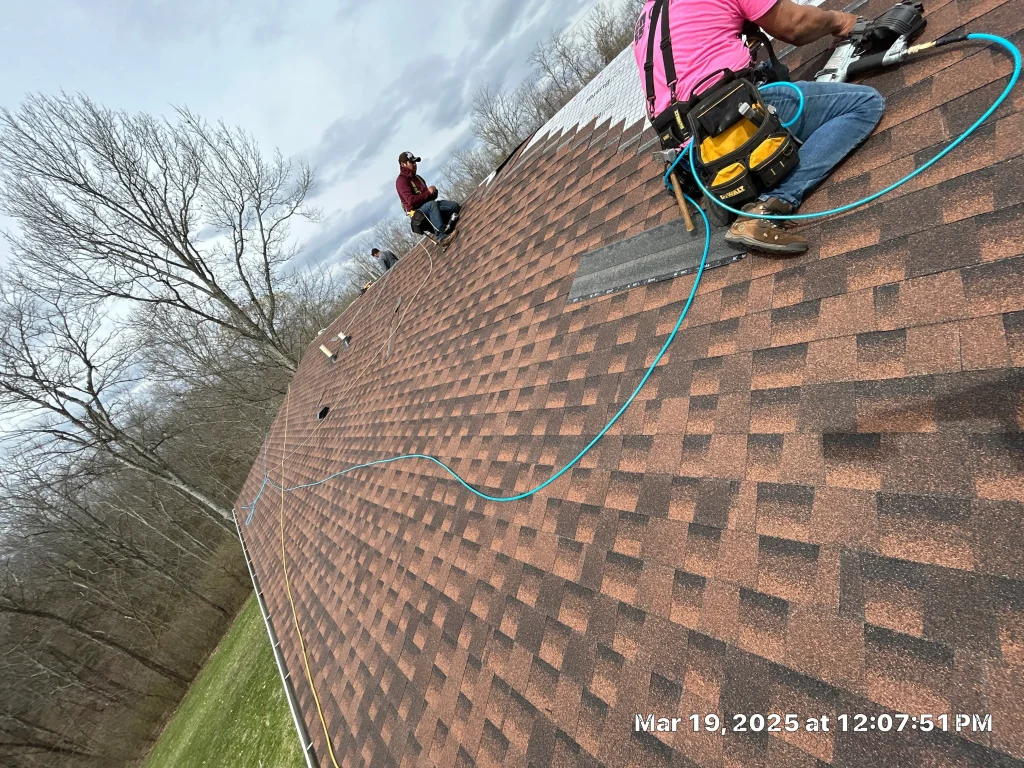 AIC Roofing crew members performing a roof repair on a steep shingle roof in Lexington, KY, using safety gear and pneumatic tools.