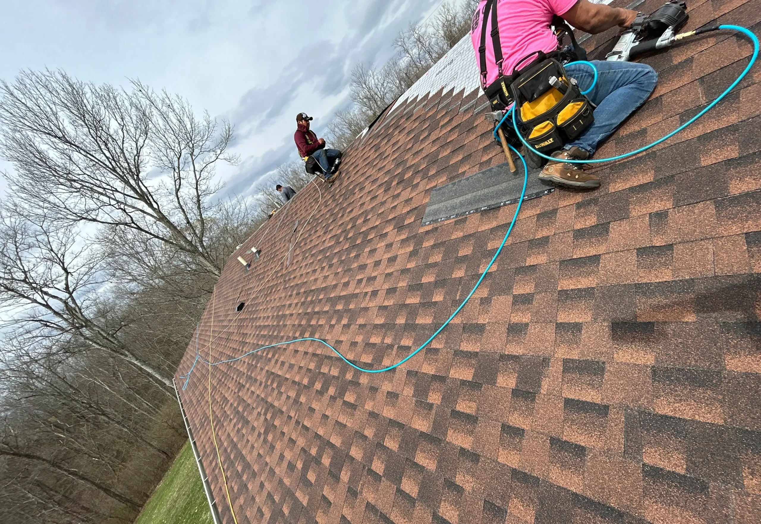Roof Repair in Progress in Lexington, KY by AIC Roofing AIC Roofing crew members performing a roof repair on a steep shingle roof in Lexington, KY, using safety gear and pneumatic tools.