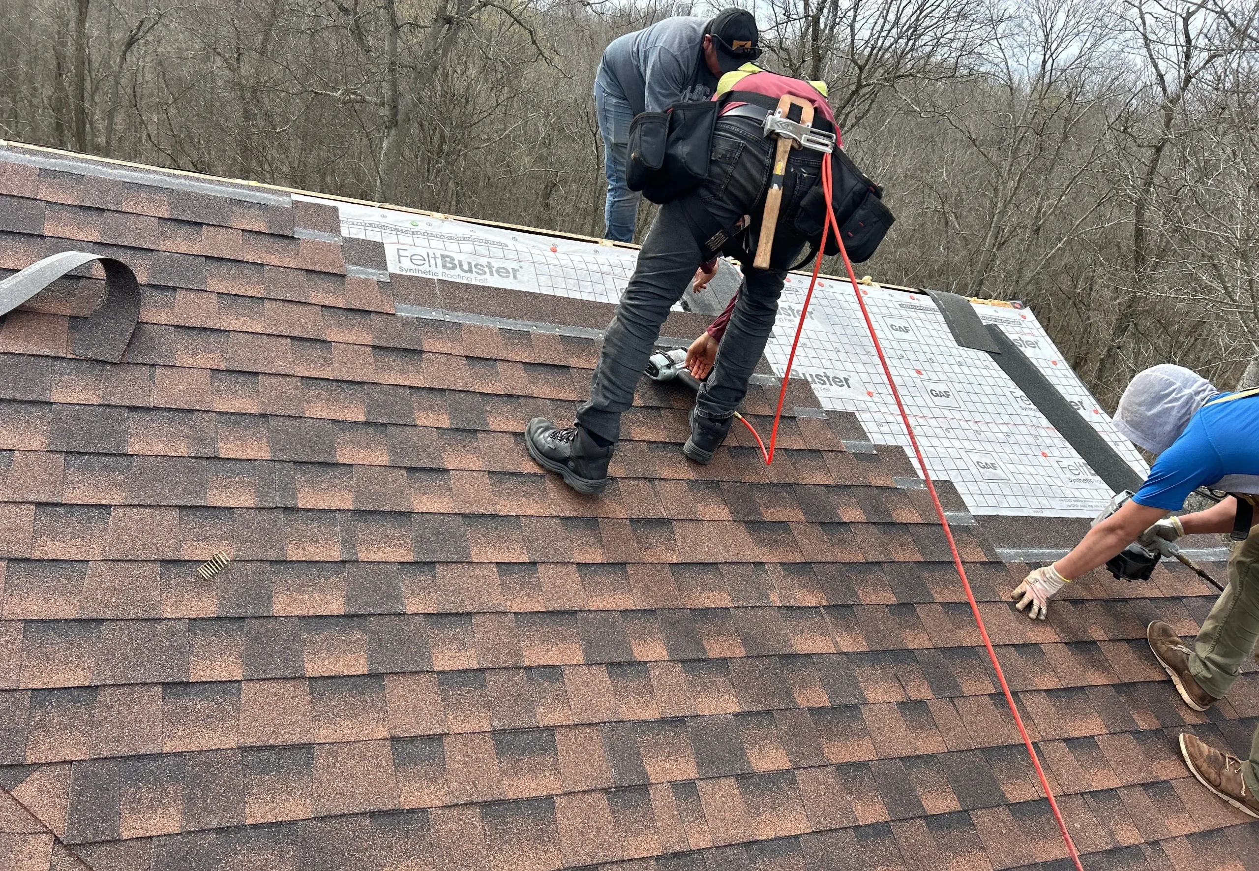 Three AIC crew members installing shingles on a residential roof in Sadieville, KY, using safety harnesses and synthetic underlayment.