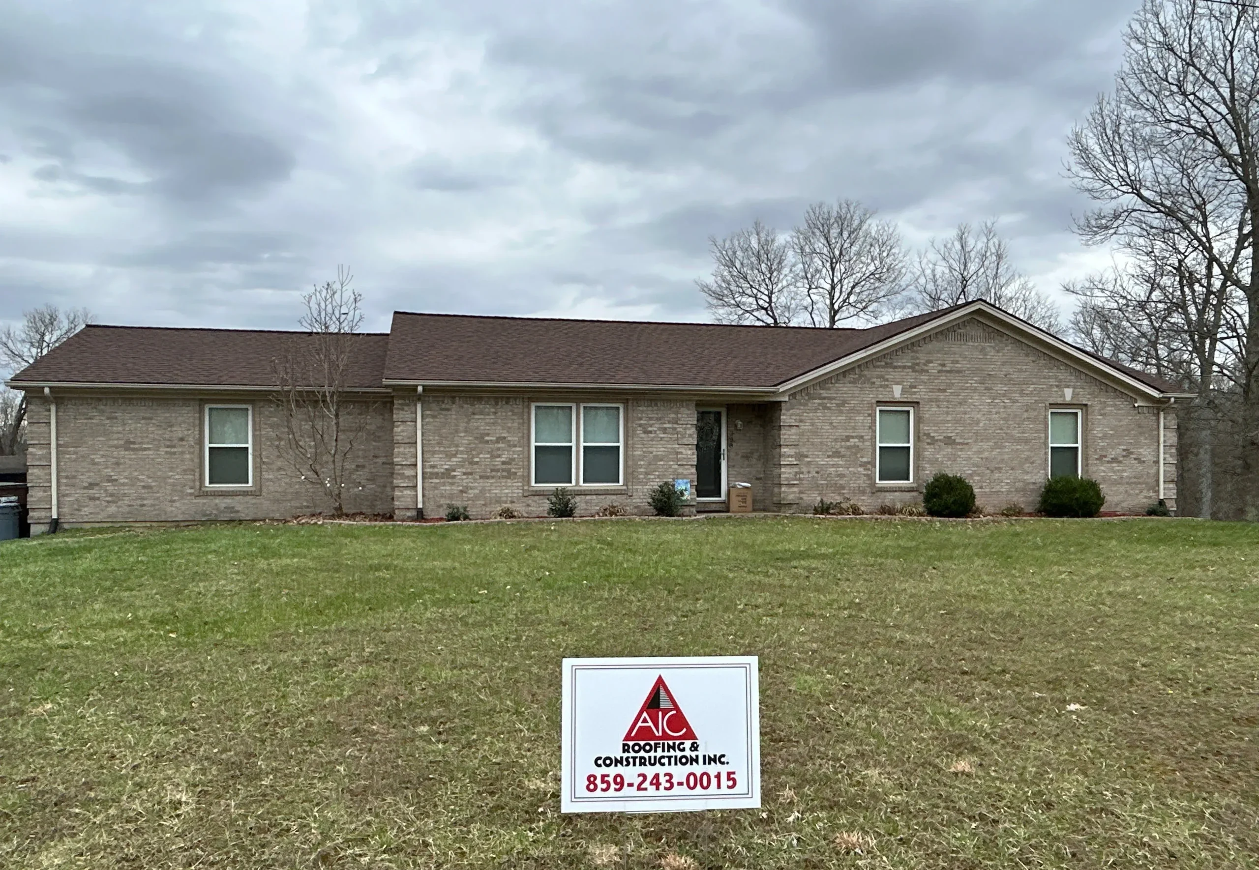 A single-story brick home in Sadieville, KY with a new roof installed by AIC Roofing & Construction, featuring a sign in the yard.