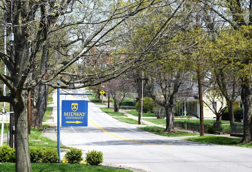 Midway University sign on a tree-lined residential street in Midway, KY