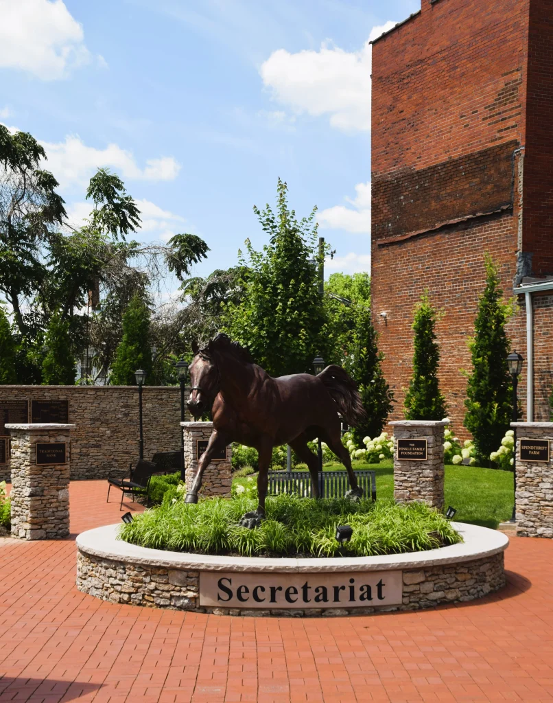 Bronze statue of Secretariat surrounded by flowers and engraved stone pedestals.