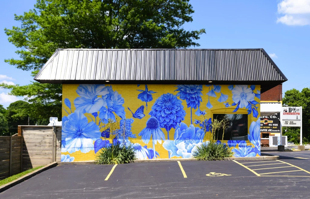 Blue floral mural on a yellow brick building with a dark metal roof in Bagdad, Kentucky.