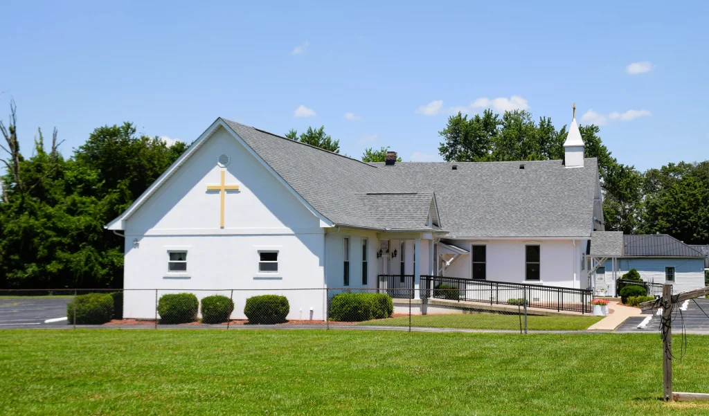 White church building with gray shingle roof and yellow cross in Buckner KY