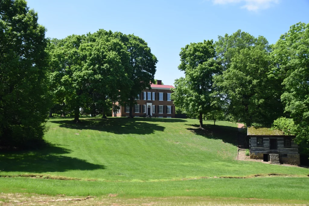 A large brick mansion surrounded by trees on a grassy hill at My Old Kentucky Home